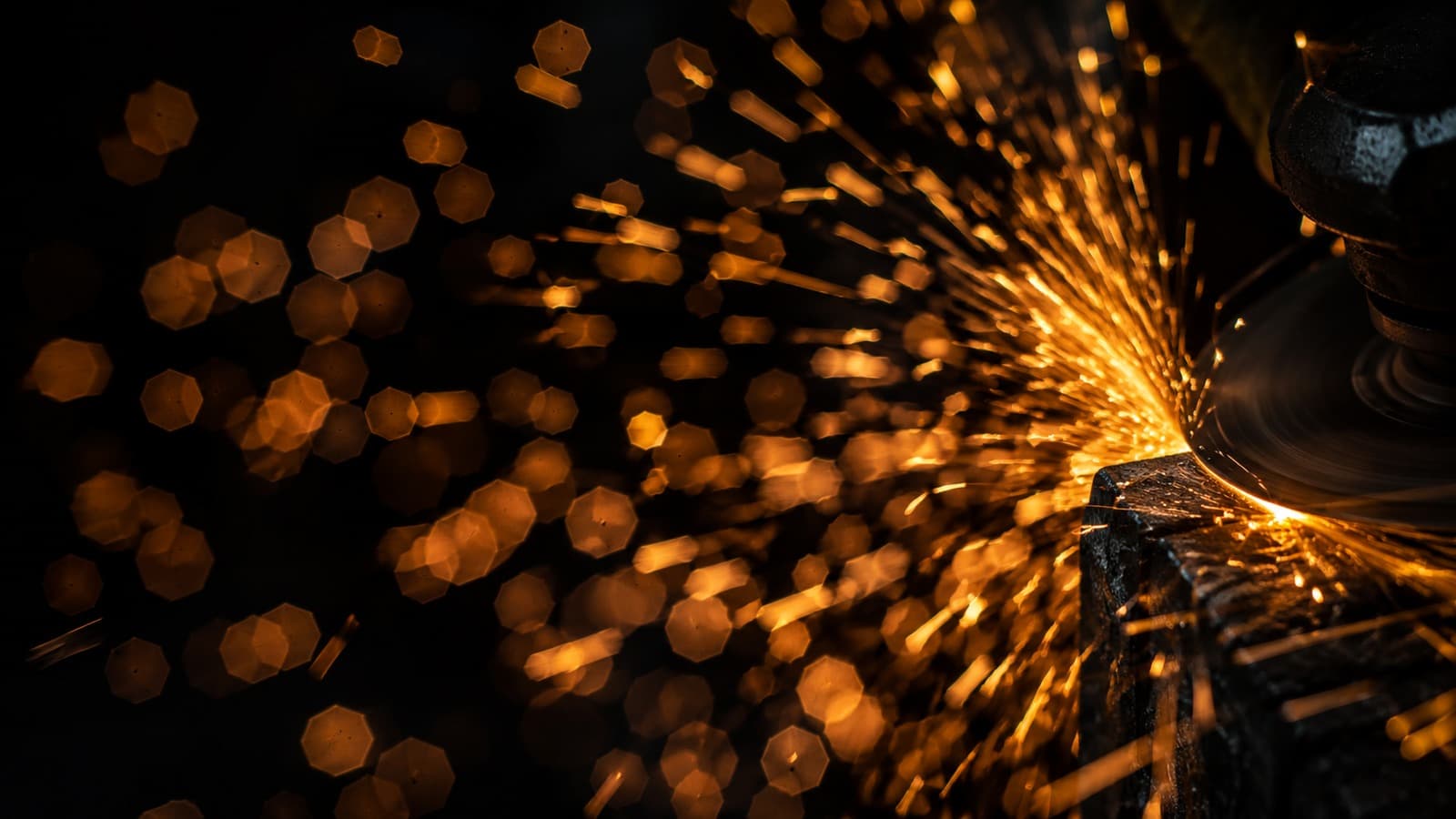 Abstrakte Amber-Funken eines Winkelschleifers vor schwarzem Hintergrund mit hexagonalem Bokeh.